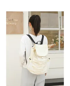 Vista posterior de una mochila de nylon plisado crema llevada por una modelo en un café
