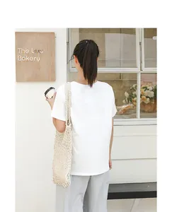 Back view of woman carrying a beige cotton mesh woven shoulder beach bag