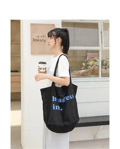 Modelo que lleva un bolso tote de lona lavada negra con letras azules en un cafe.