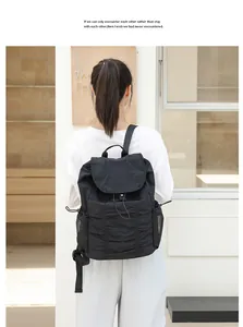 Vista trasera de modelo con mochila de nailon negro plisado con solapa y cordones