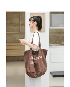 Elegante bolso de lona marrón lavado con estampado de letras blancas mostrado en una modelo
