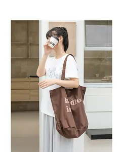 Foto de estilo de vida de un bolso tote de lona lavada marrón con letras sobre una modelo.