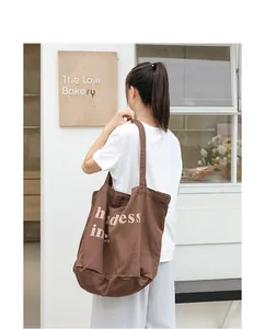 Bolso tote tipo cubo de lona marrón vintage con letras impresas al hombro de una modelo