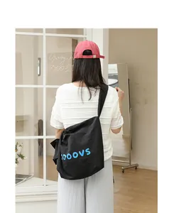 Detail of a black nylon crossbody bag with blue lettering on a casual model outfit.