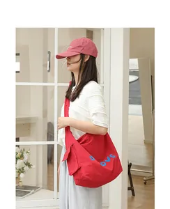 Side view of a red canvas crossbody bag featuring knotted strap and blue letters