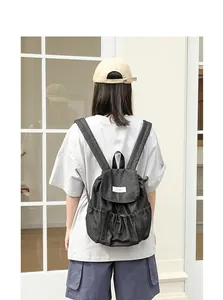 Vista trasera de una mochila vaquera negra con cordón usada por una modelo en exteriores.