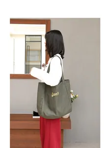 Mujer con bolso tote de lona verde oscuro con detalles de bordado amarillo en primer plano