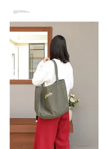 Primer plano del bolso tote de lona verde con el logotipo bordado de Super Dog amarillo.