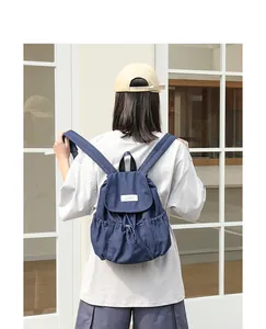 Vista detallada de una mochila de lona azul marino con cordón usada por un modelo casual.