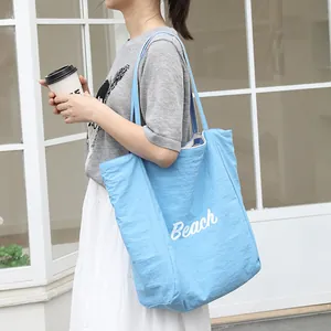 Elegante bolso tote de nailon azul con estampado 'Beach' llevado por una mujer en el exterior.