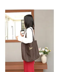 Bolso tote de lona marrón con bordado dorado llevado por modelo en estilo casual