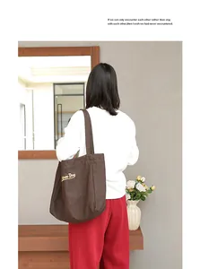 Vista detallada de un bolso tote de lona marrón con bordado Super Dog llevado por una modelo.