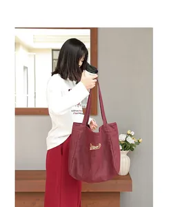 Bolso tote grande de lona burdeos con bordado amarillo sostenido por modelo