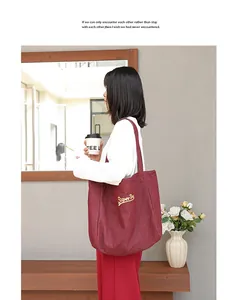 Vista lateral del bolso tote de lona burdeos con bordado amarillo llevado por modelo