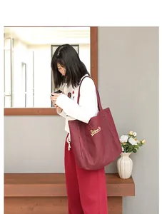 Detalle de bolso tote de lona burdeos con logotipo bordado en modelo femenina