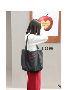 Bolso tote casual de lona negra con bordado rojo Super Dog en el hombro del modelo.