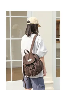 Modelo femenina con una mochila de lona marrón vintage con cordón y detalles plisados.