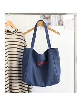 Detalle de un bolso tote denim azul con bordado Super Dog rojo en un colgador de ropa
