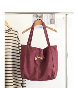 Detalle de un bolso tote de lona burdeos con bordado amarillo SuperDay colgado de una percha