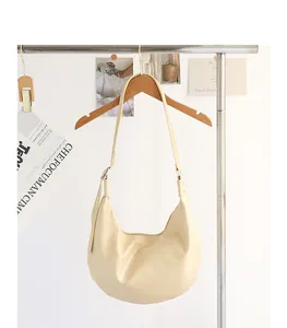 Detalle de un bolso hobo minimalista de piel sintética suave crema colgado de un soporte