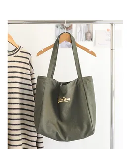 Detalle de bolso tote de lona verde con bordado Super Dog colgado en un perchero.