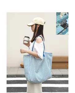 Side view of a large blue and white striped nylon tote bag carried by a model on street
