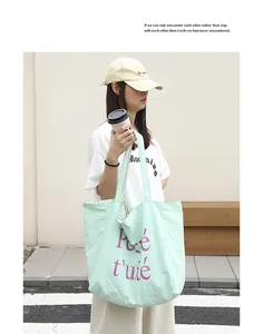 Model carrying a mint green nylon tote bag featuring purple letter print design