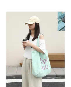Street style mint green nylon tote bag with purple letter print carried by model