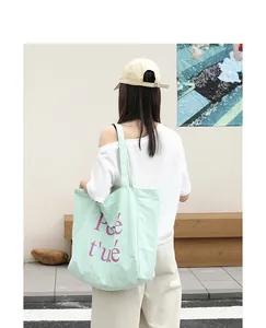 Close-up of a light green nylon tote bag with purple letter print on model's shoulder