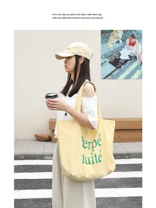 Large yellow nylon tote bag with green letter print carried by a model outdoors