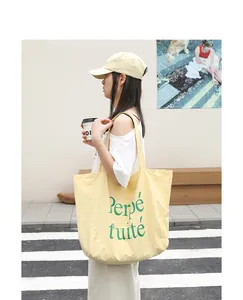 Detailed lifestyle view of a large yellow nylon tote bag featuring green letter print