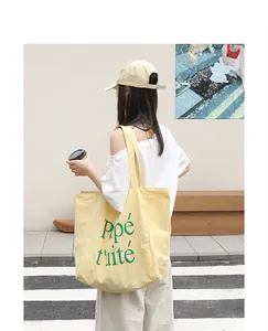 Close-up detail of the yellow nylon tote bag featuring green letter print in outdoor setting