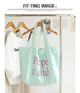 Close-up detail of a mint green nylon tote bag with pink letter print hanging on a rack