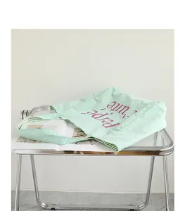 Stylish mint green nylon tote bag with purple lettering on a modern glass table