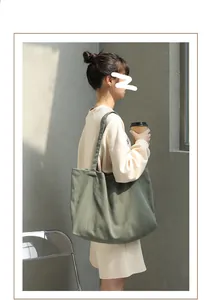 Model wearing an olive green minimalist canvas tote bag in a lifestyle setting.