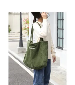 Primer plano de un bolso de hombro de pana verde con bordado de letras blancas casuales