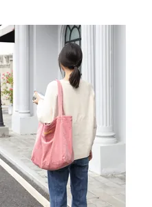Bolso de hombro de pana rosa con letras bordadas amarillas llevado por una modelo