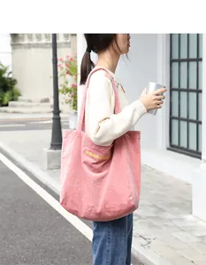 Detalle de un bolso tote de pana rosa con bordado amarillo para un look casual.
