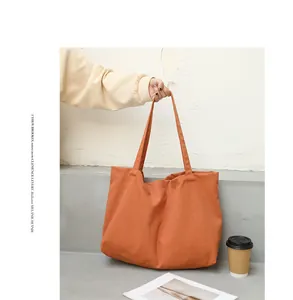 Detail view of a burnt orange canvas tote bag held by hand in a minimalist setting