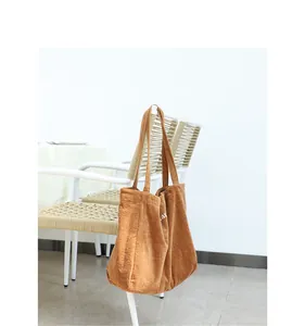 Bolso tote de pana marrón con bordado de letras blancas colgado en una silla blanca