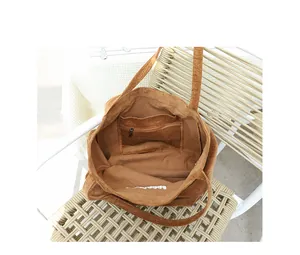 Vista interior de un bolso tote de pana marrón con bolsillo interno con cremallera y bordado.