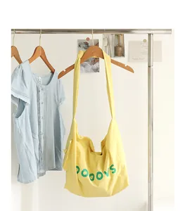 Vibrant yellow nylon crossbody bag featuring green letter print and decorative knot strap detail