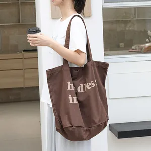 Bolso tote de lona marrón grande con estampado de letras llevado por una modelo joven