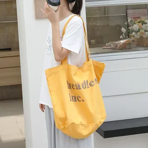 Elegante bolso tote de lona amarilla con estampado de letras llevado al hombro de