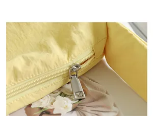 Close-up detail showing the silver metal zipper puller on a yellow nylon crossbody bag