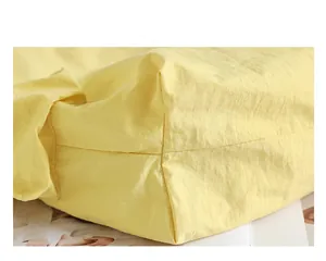 Detailed macro shot of the bottom corner and crinkled texture of a yellow nylon tote bag.