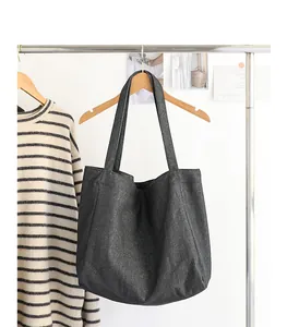 Bolso tote vintage de lona vaquera gris oscuro colgado en una percha de madera minimalista