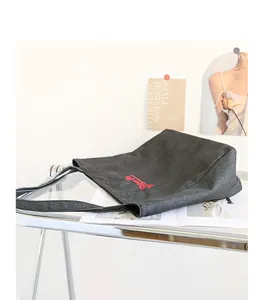 Primer plano de un bolso tote de lona denim negra con logo cursivo bordado en rojo.