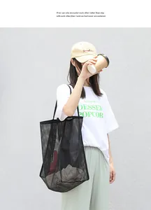 Bolso de malla negra llevado por una modelo frente a una pared blanca con textura