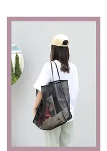 Bolso bandolera de malla negra informal llevado por una modelo ante una pared grisácea